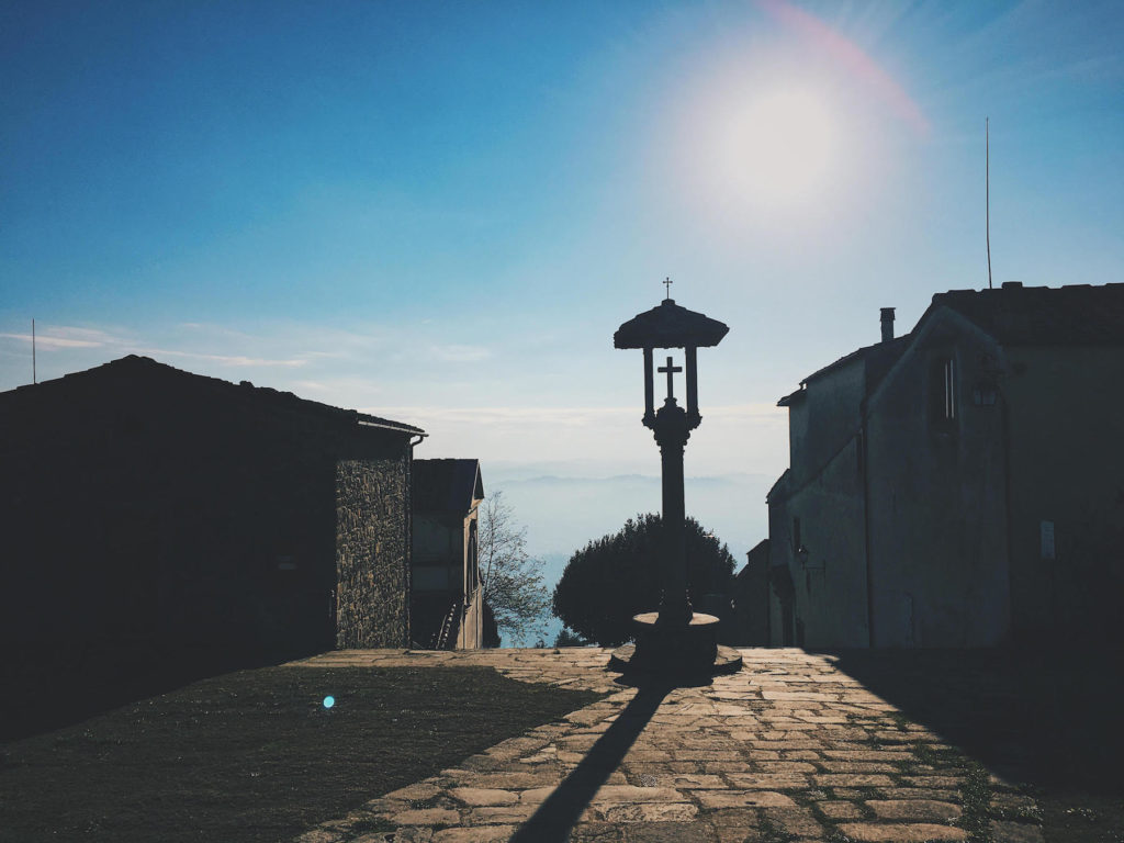 Cross post overlooking clouds and old buildings